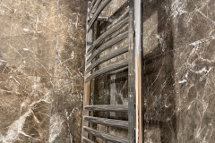 Detail of chrome ladder radiator in marble tiled walk in shower