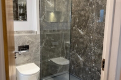 View of monochrome bathroom with walk in shower with glass partition and wall hung white toilet